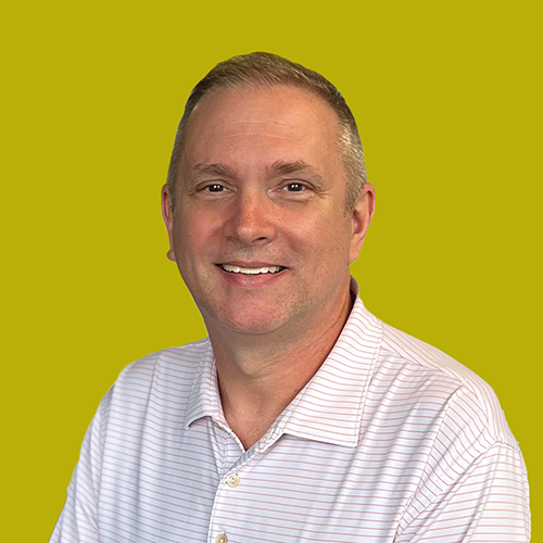 Smiling man wearing a light-colored, short-sleeve, collared shirt poses in front of a solid yellow-green background.