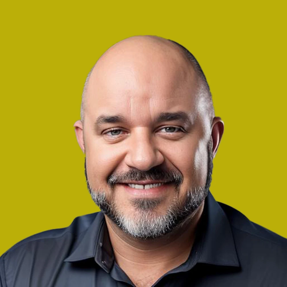 Smiling bald man with a short gray beard wearing a dark shirt, posed against a plain yellow background.