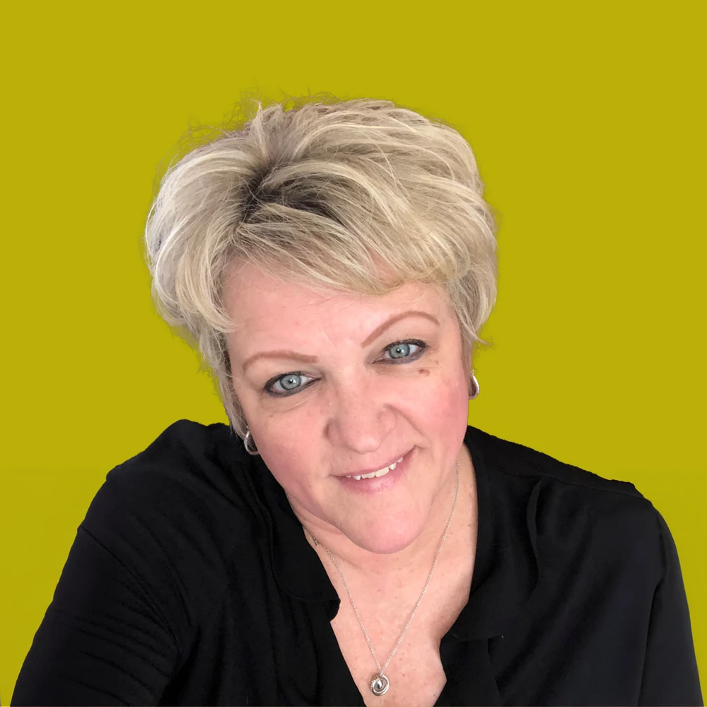 Woman with short blonde hair, blue eyes, and a black top, smiling slightly against a solid yellow-green background.