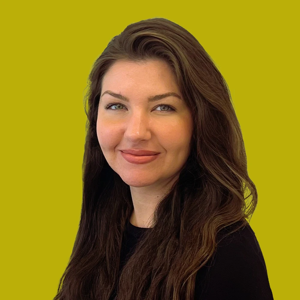 Woman with long brown hair and a black top smiling in front of a solid yellow background.
