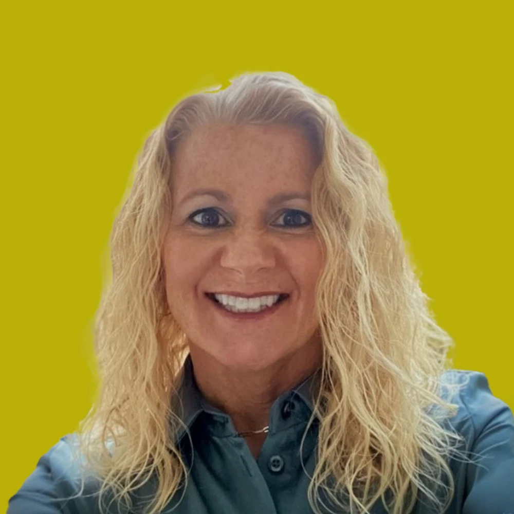 Smiling woman with wavy blonde hair wearing a teal collared shirt, posed against a solid yellow background.