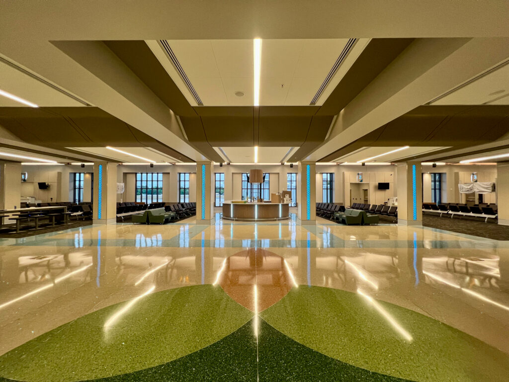 Empty airport gate area with a central information desk, rows of seating, and a decorative terrazzo floor.